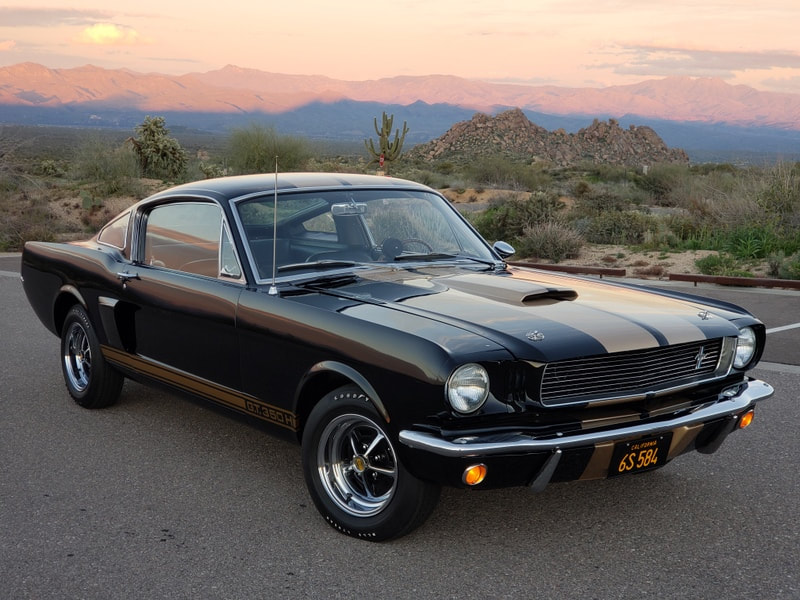 Classic black 1960s muscle car parked on a desert road at sunset.