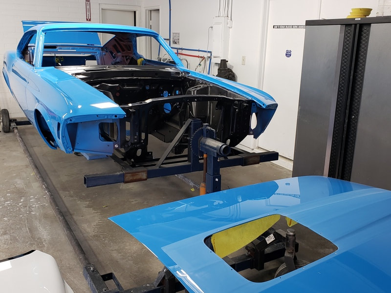 A blue car body undergoing restoration in a garage.