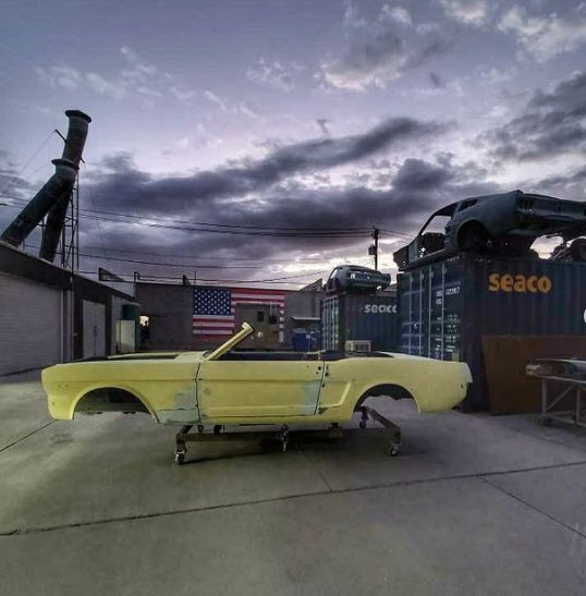 A yellow car body shell in an industrial outdoor setting at dusk.