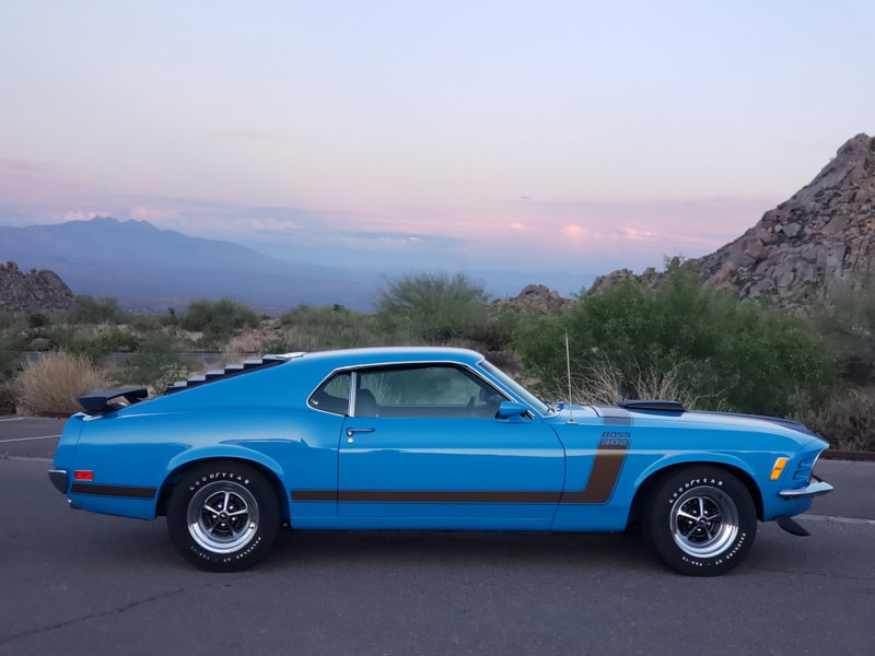A classic blue muscle car parked with mountains in the background at dusk.