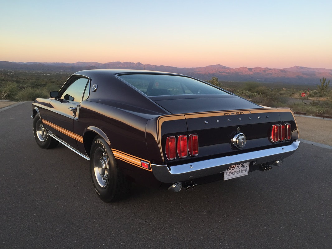 Classic black Ford Mustang parked on a road at sunset.