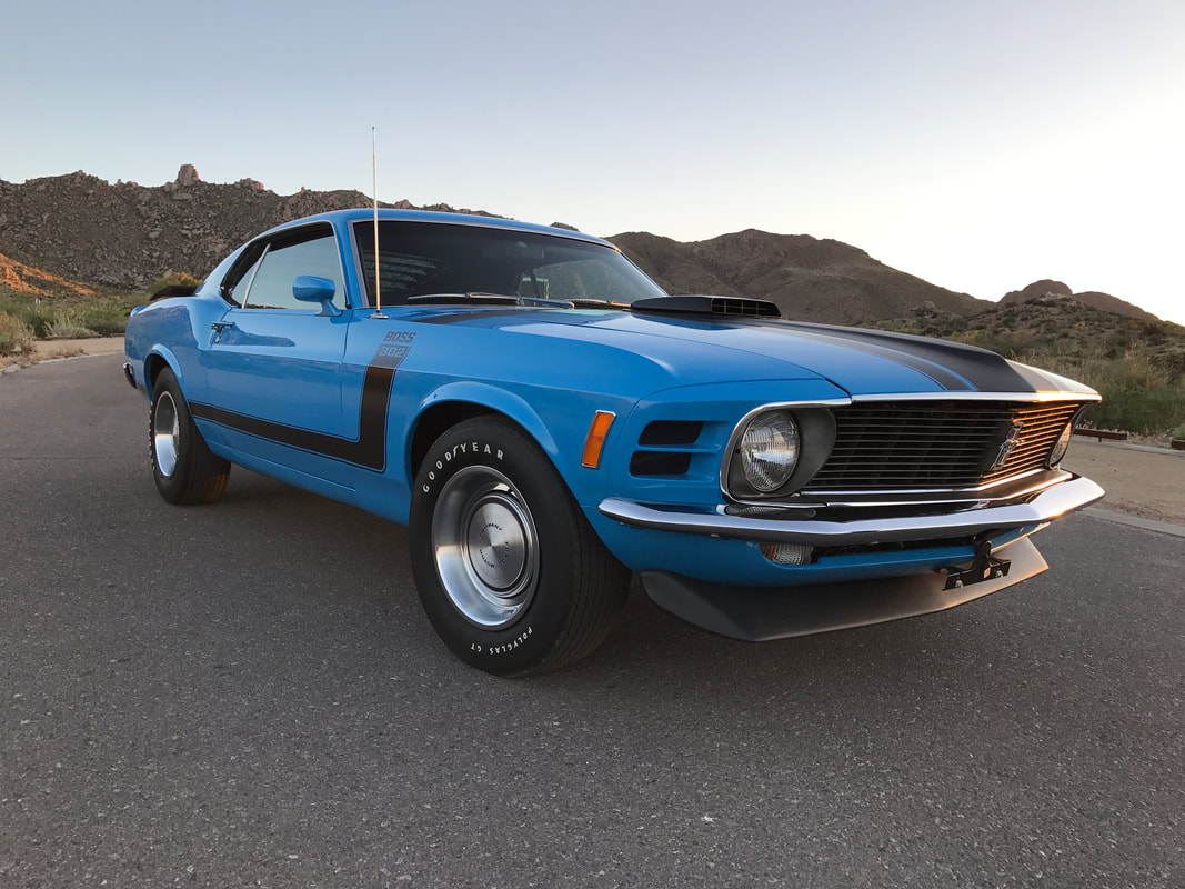 Blue vintage muscle car parked on a road with mountainous background.