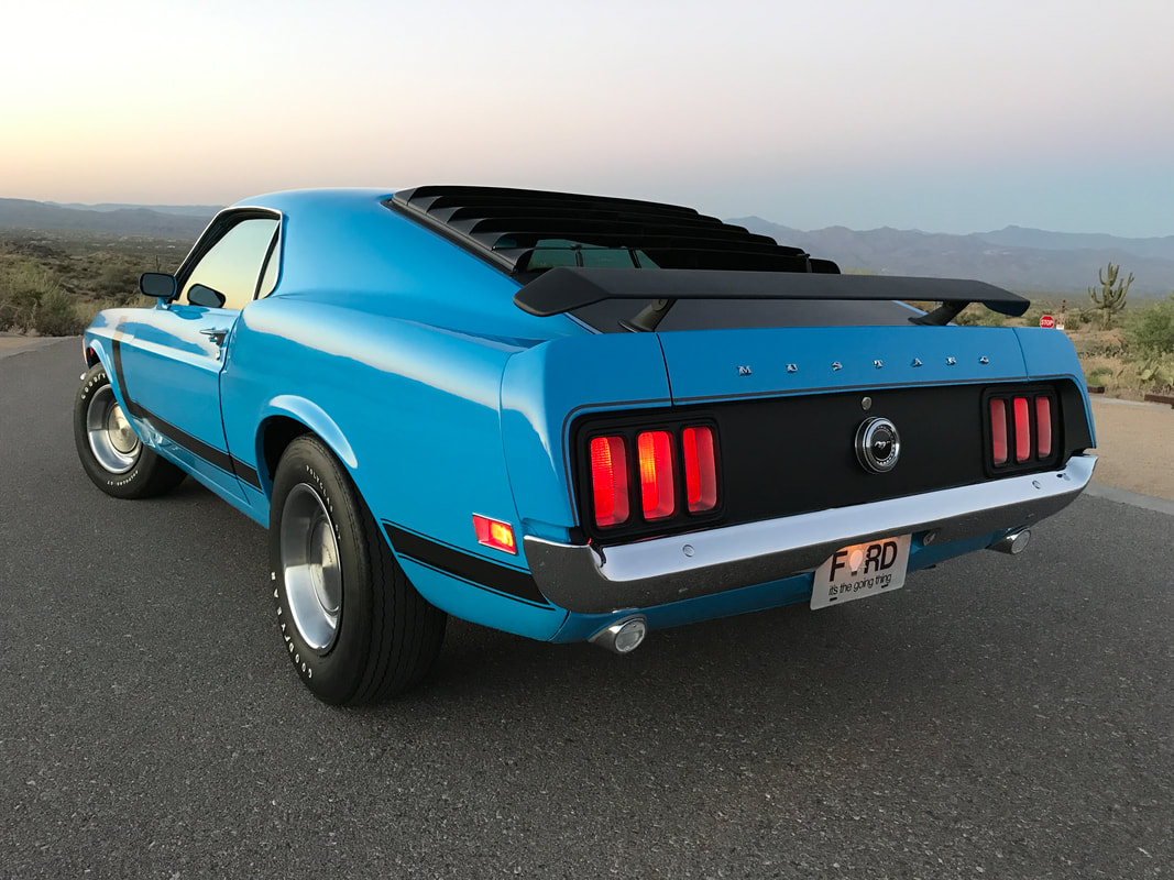 A blue vintage Ford Mustang parked on an open road during sunset.