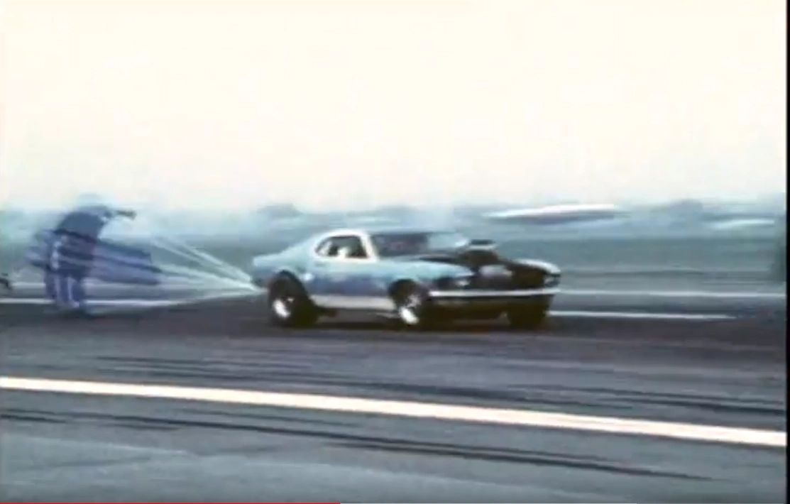 Drag racing car deploying parachute on track.