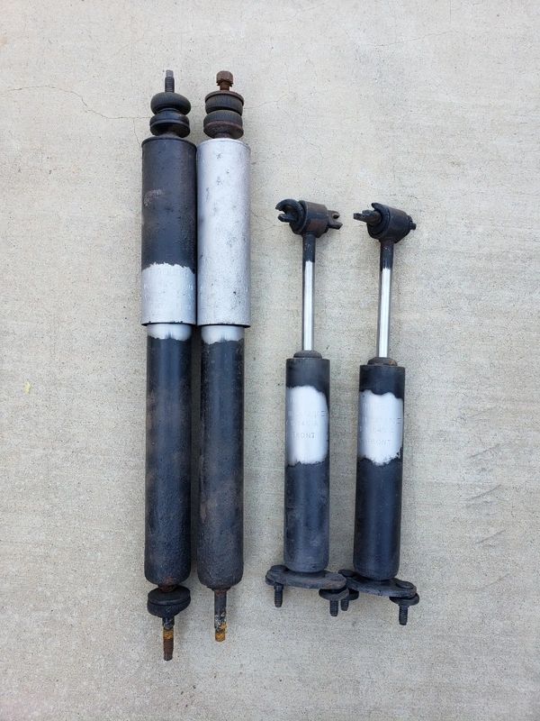 Four used car shock absorbers on ground.