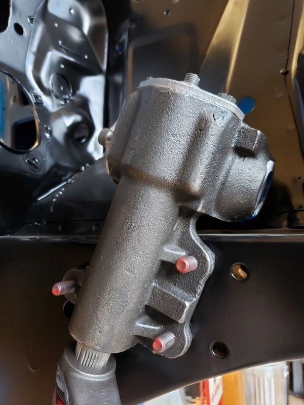 Metal steering box mounted on vehicle frame.