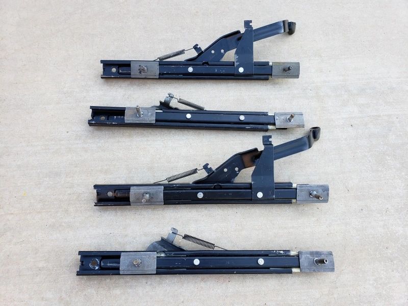 Four metal seat slider mechanisms on concrete.