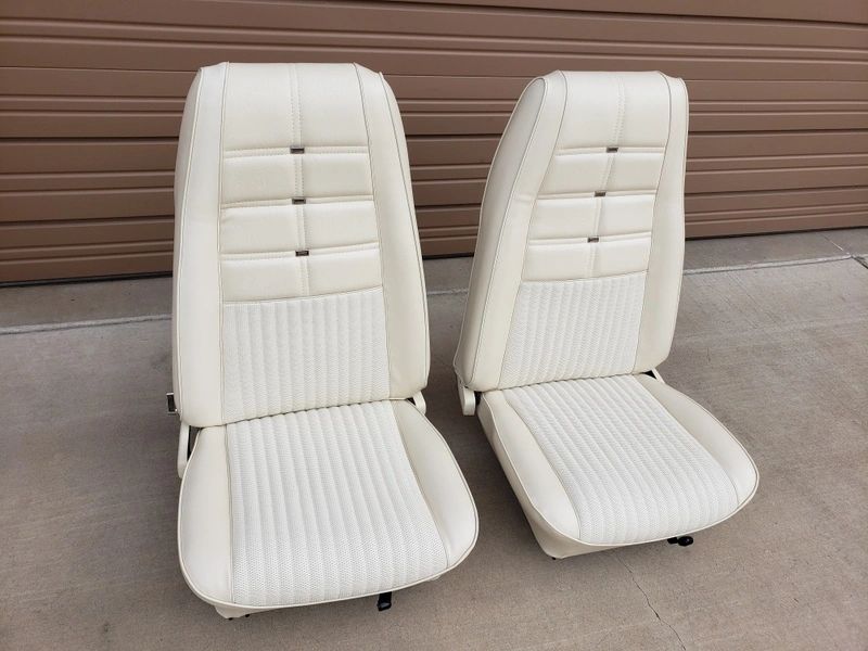 Two white car seats on concrete ground.