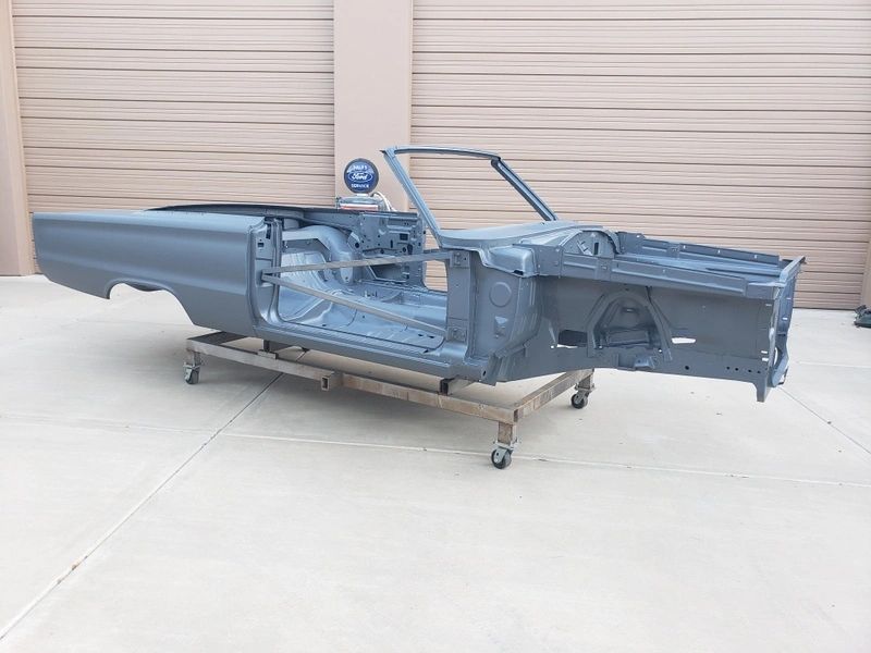 Car chassis on wheeled platform outside garage.