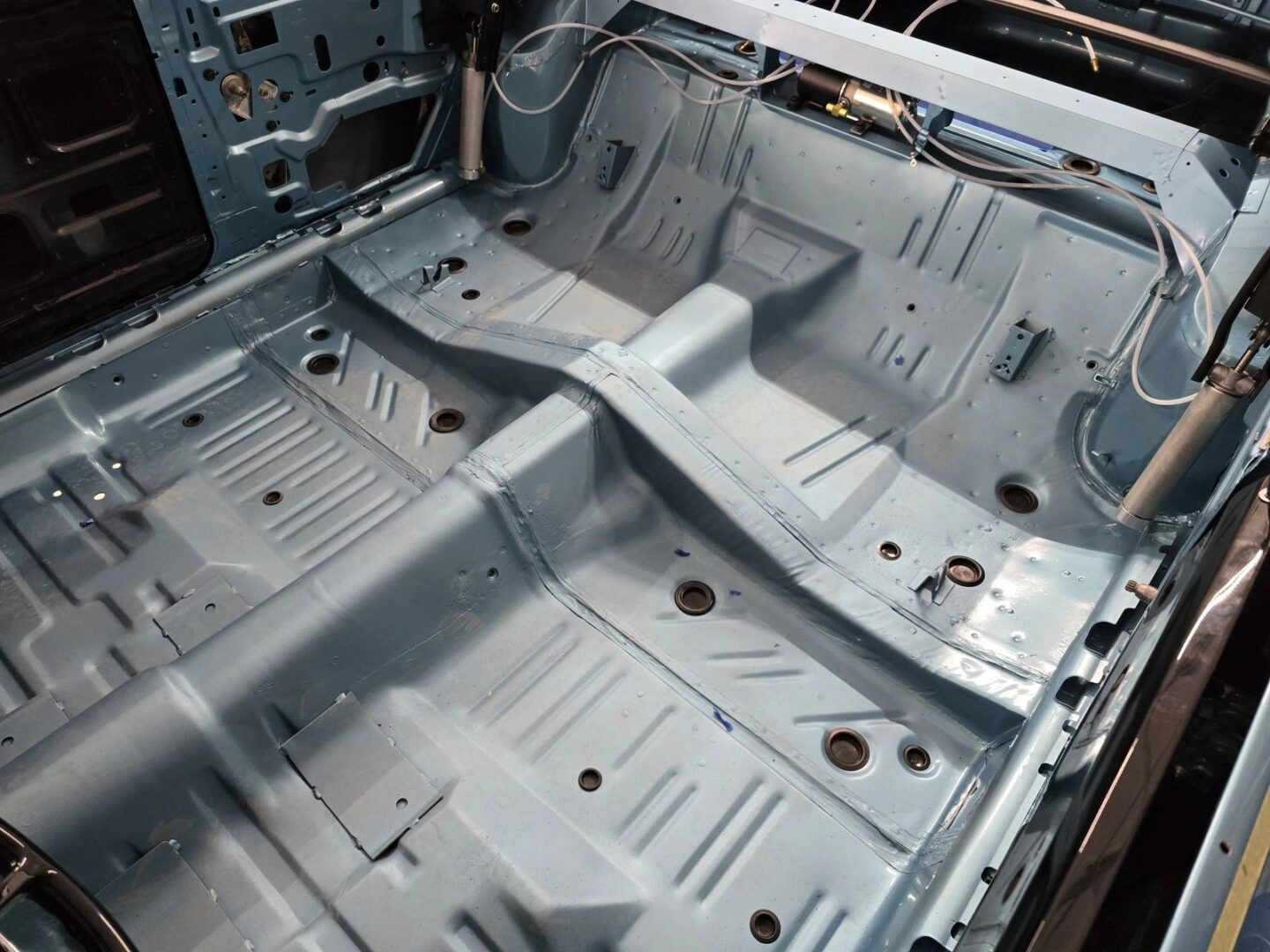 Car interior floor with metal chassis exposed.