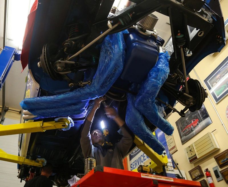 Mechanic working on car underbody in garage.
