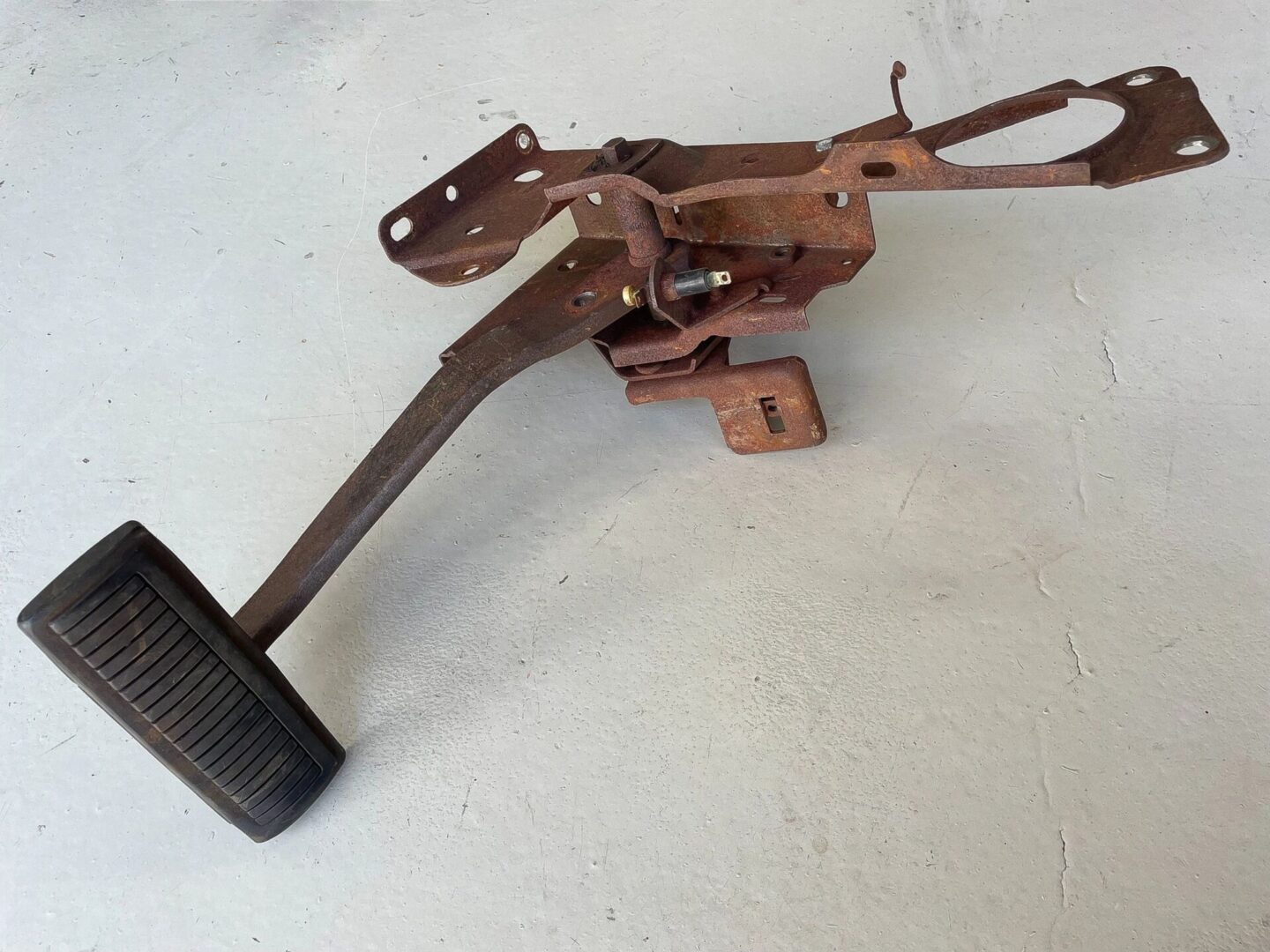 Rusty car brake pedal assembly on floor.