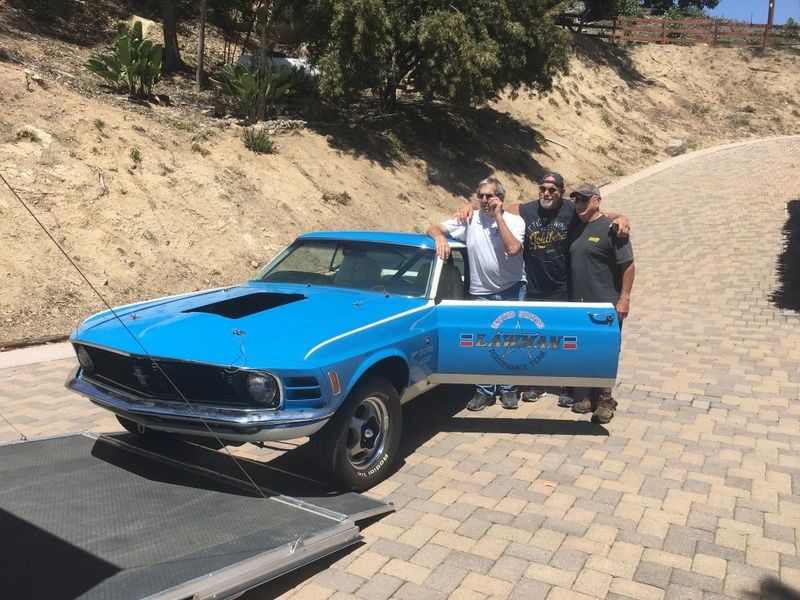Three people with a classic blue car.
