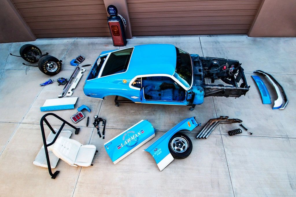 Disassembled blue car parts on concrete floor.