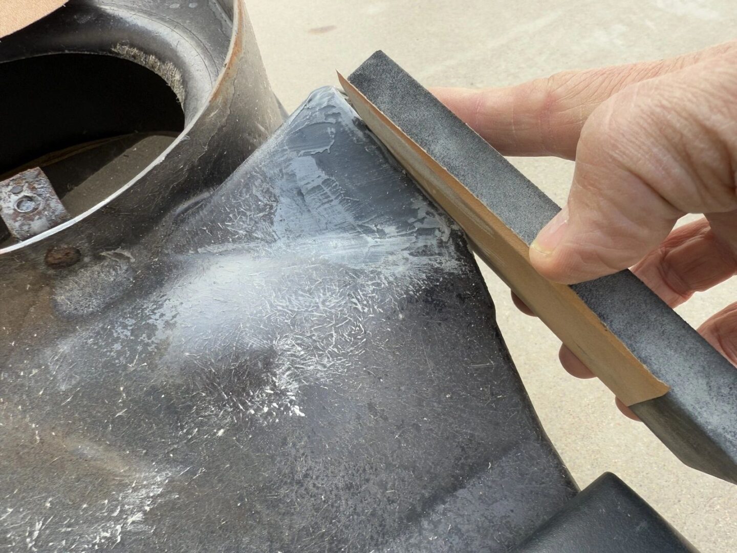 Sanding a metal surface with sandpaper block.