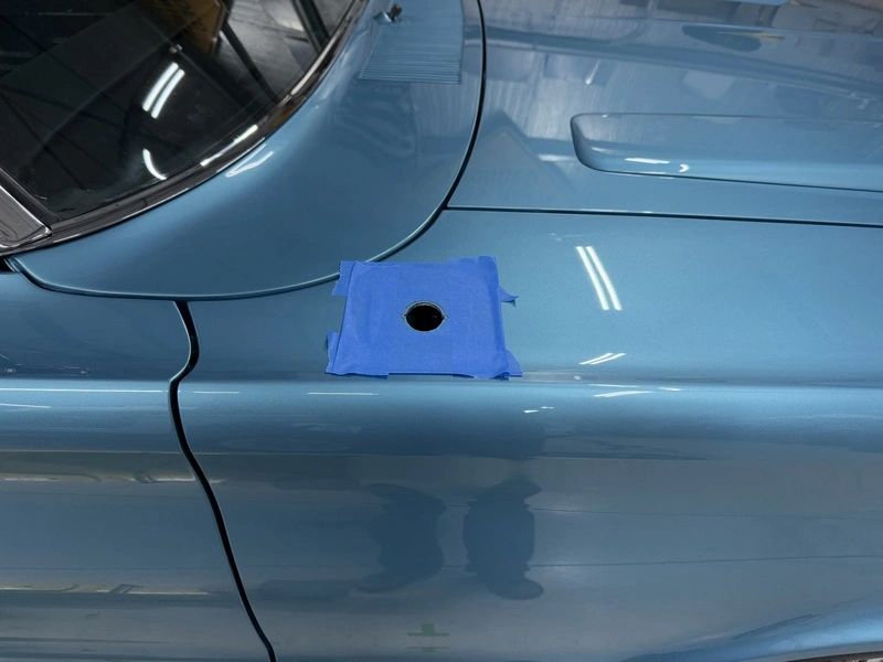 Blue car with taped hole on hood.