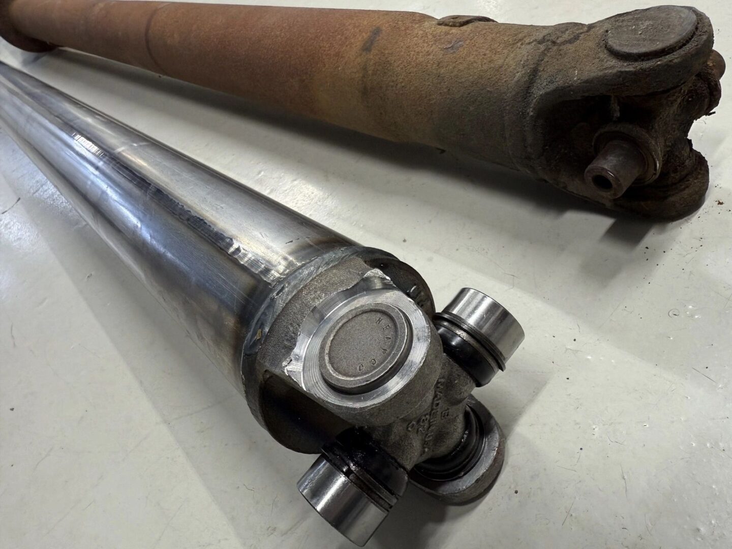 Two car driveshafts, one rusty, one shiny.