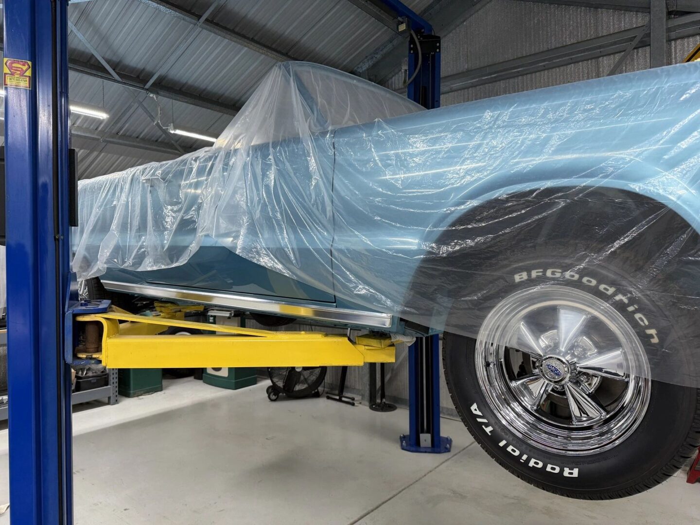 Classic car covered in plastic on lift.
