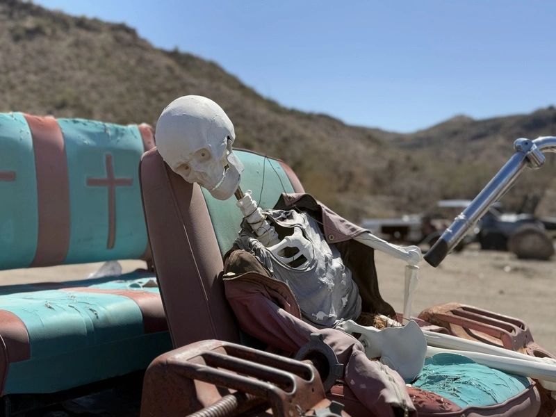 Skeleton sitting on abandoned car seat outdoors.