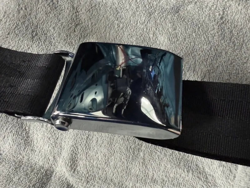 Chrome seatbelt buckle on textured fabric.