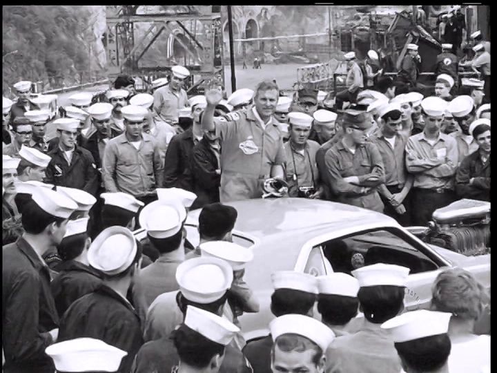 Crowd of sailors gathered around a car.