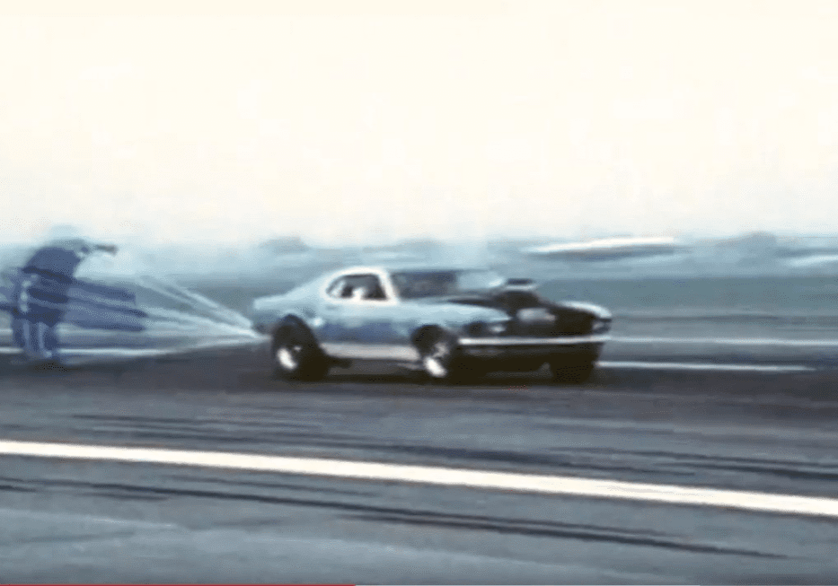 Drag racing car deploying parachute on track.