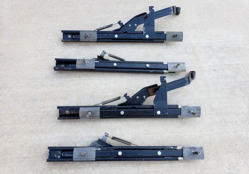 Four metal seat slider mechanisms on concrete.