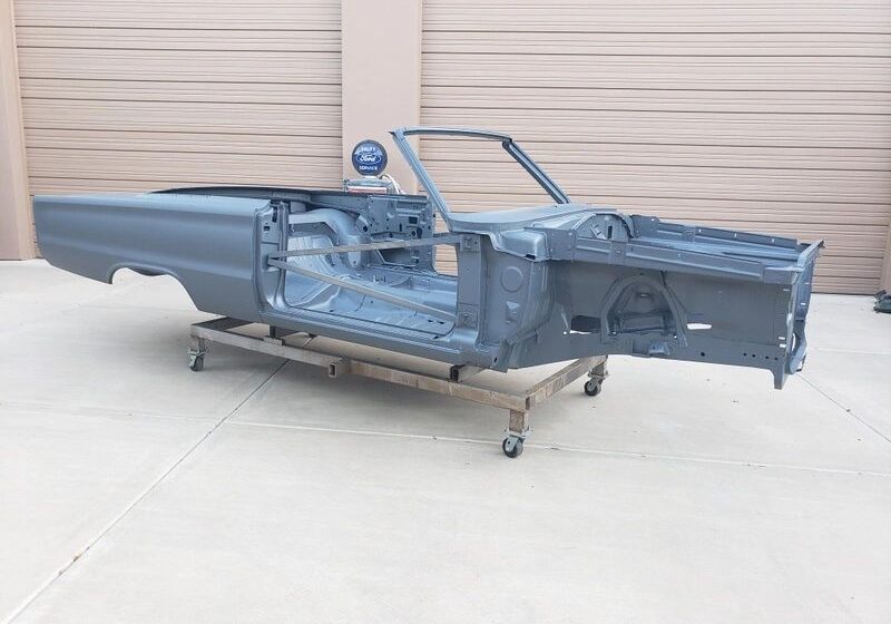 Car chassis on wheeled platform outside garage.