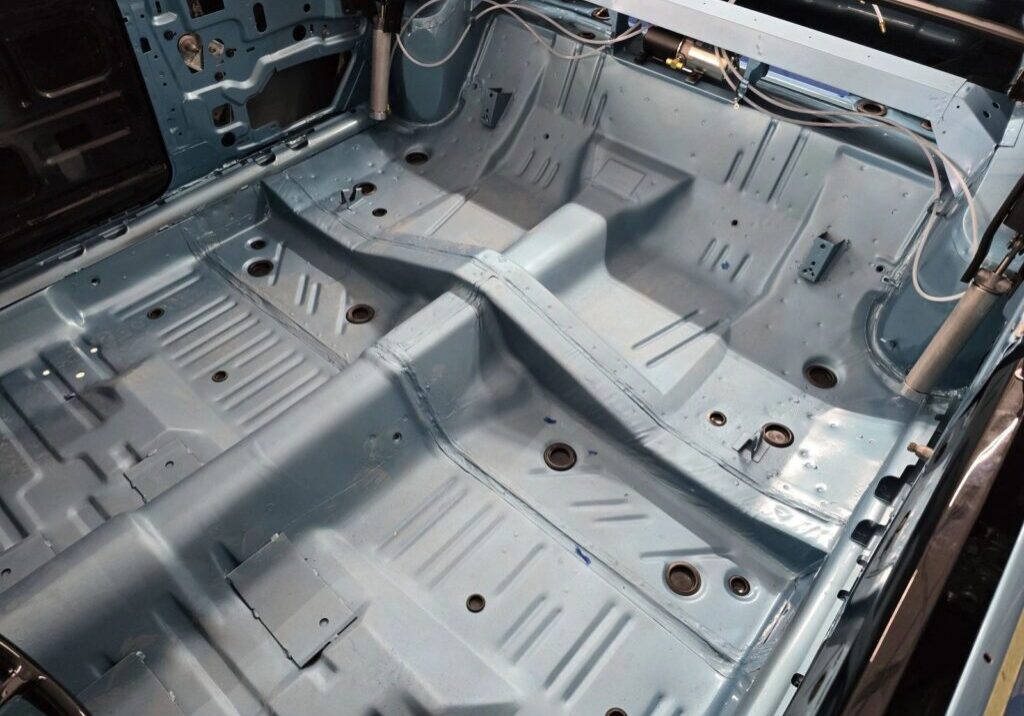 Car interior floor with metal chassis exposed.