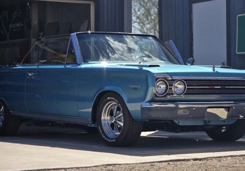 Blue classic convertible car parked outside garage.
