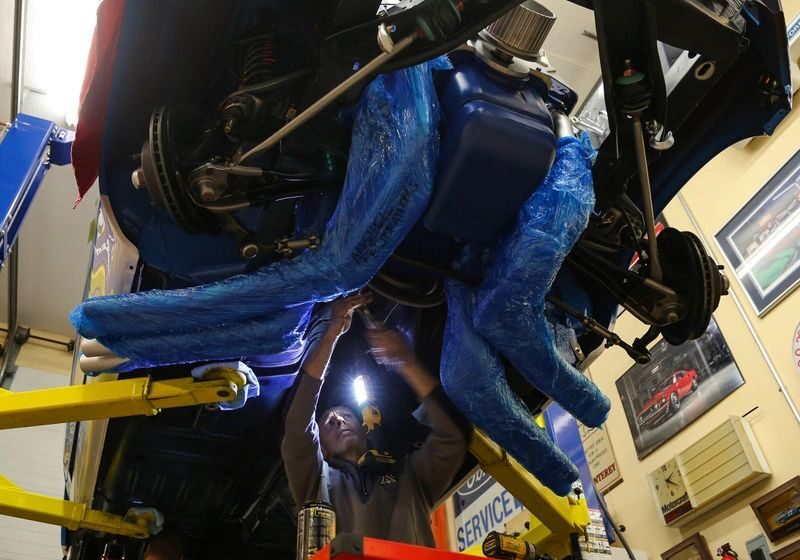 Mechanic working on car underbody in garage.