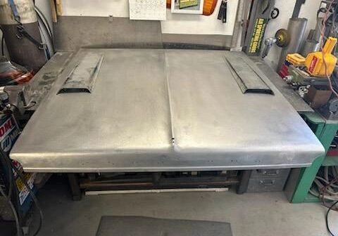 Metal car hood on workshop table.