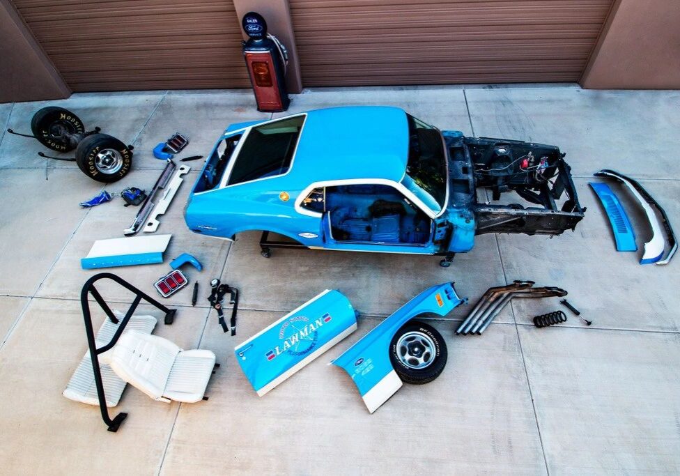 Disassembled blue car parts on concrete floor.