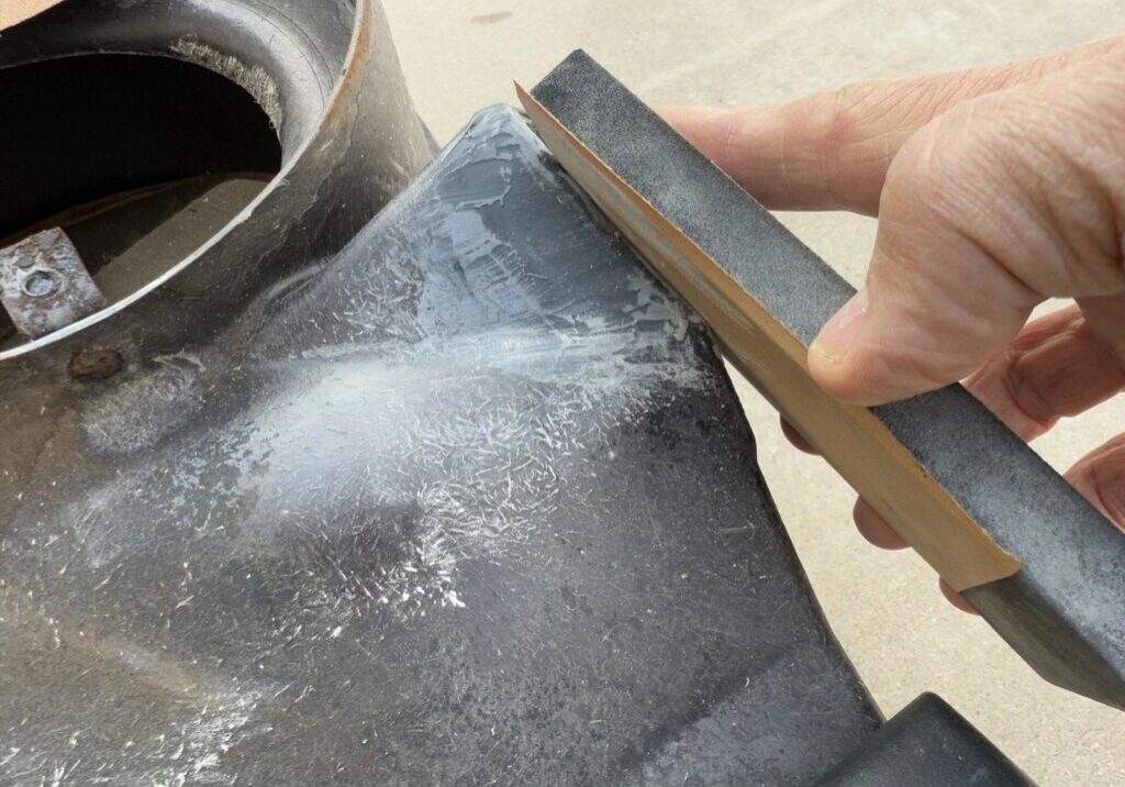Sanding a metal surface with sandpaper block.