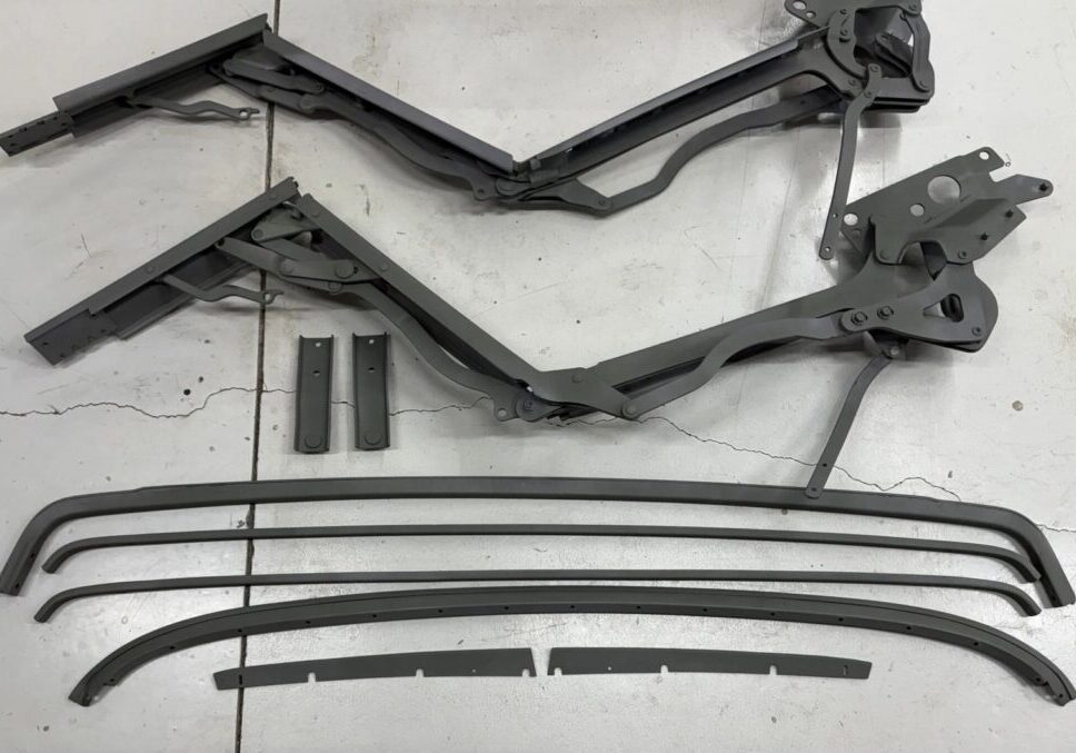 Convertible car top frame parts on floor.