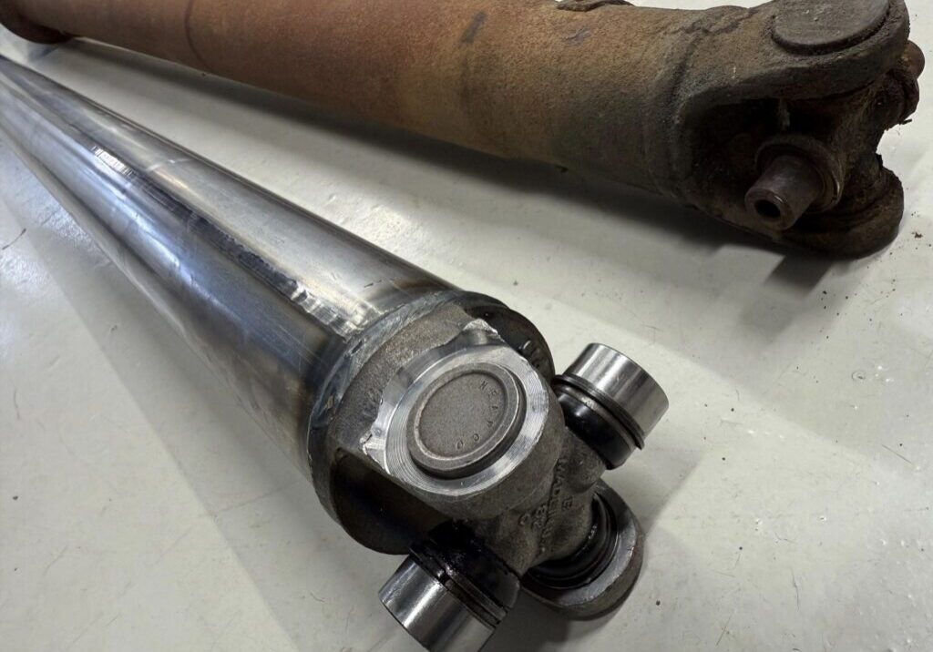 Two car driveshafts, one rusty, one shiny.
