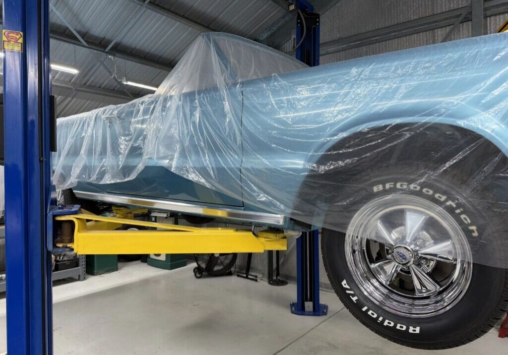 Classic car covered in plastic on lift.