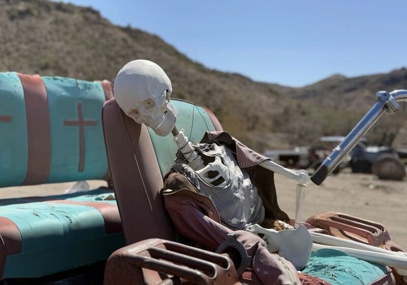 Skeleton sitting on abandoned car seat outdoors.