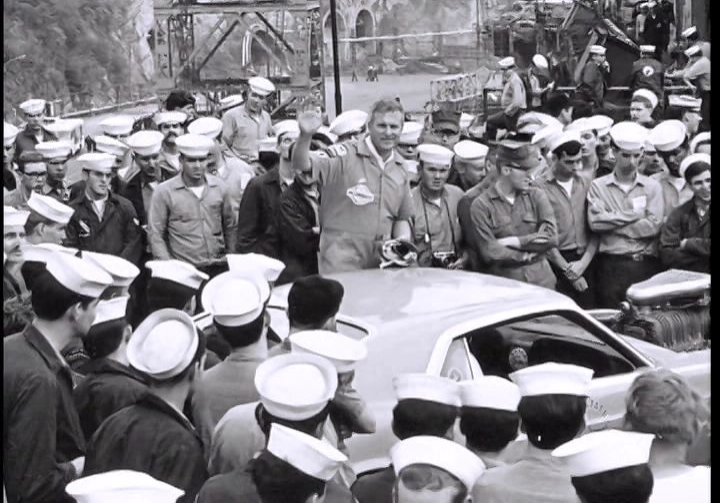 Crowd of sailors gathered around a car.